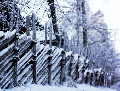 Old-fashioned wooden fence covered in snow on a cold winter day