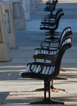 Row of several black benches on concrete walkway