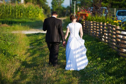 Young married couple holding hands and walking away on a countryside trail