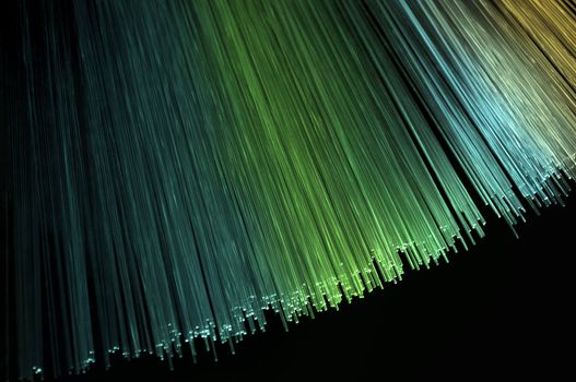 Abstract style close up capturing the ends of many green and blue illuminated fiber optic light strands arranged over black.