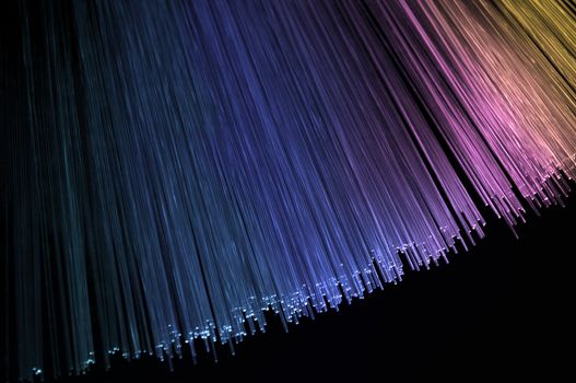 Abstract style close up on the ends of many pink, blue and violet illuminated fiber optic light strands arranged over black.