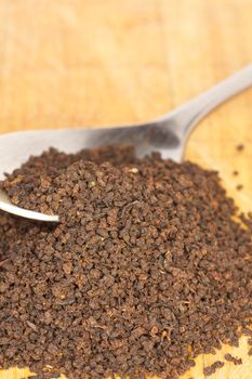 Loose black tea leaves spill from a spoon onto a wooden surface