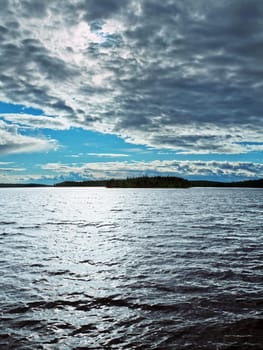 The sun through clouds shines cold waters of northern lake