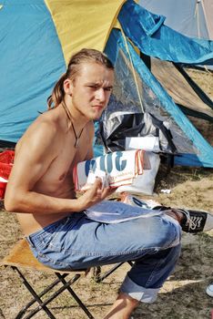 The young guy sitting on a chair near tent in forest