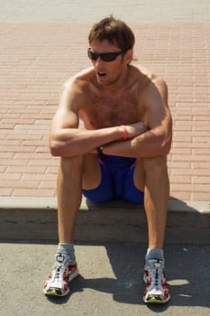 The young strong sportsman  a rest on the brink of road