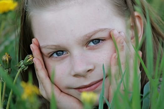 Portrait of nice, young girl in the dandelion meadow on summer day.