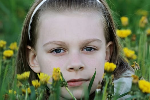 Portrait of nice, young girl in the dandelion meadow on summer day.
