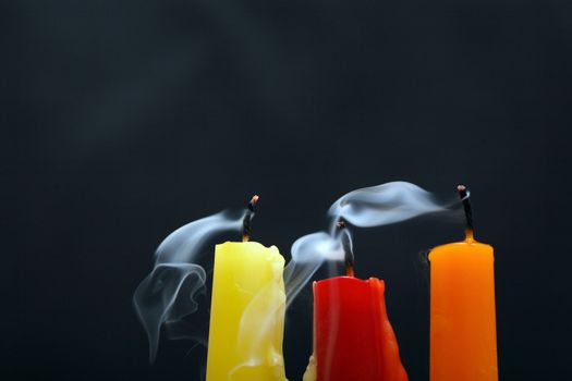 Three colored extinguished  candles with smoke on black background