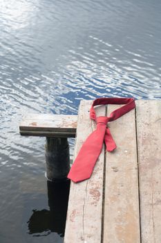 Concept with red necktie lying on wooden pier on background with river