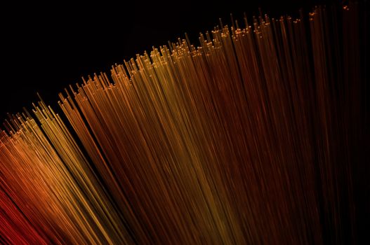 Close up on many illuminated gold, red and orange fiber optic light strands arranged over black
