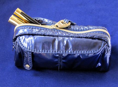 A midnight blue makeup bag with mascara, concealer and eyeliner on a matching blue background.                       