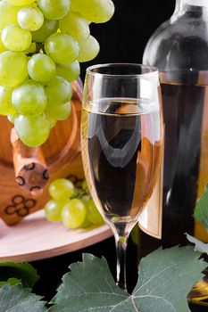 White wine bottle, glass and cask with grapes over black