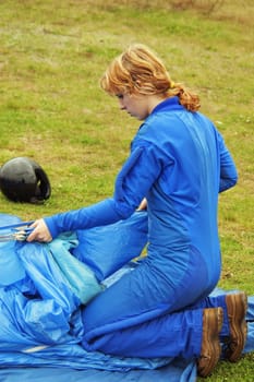 The girl-parachutist in blue overalls  prepares a parachute for a jump
