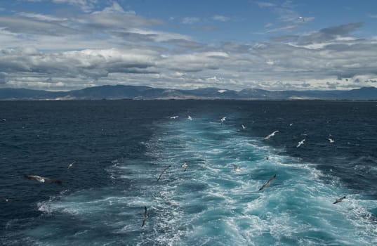 Distant view of coastline of Greece, clouds, foaming waves and seagulls - view from a ferry.