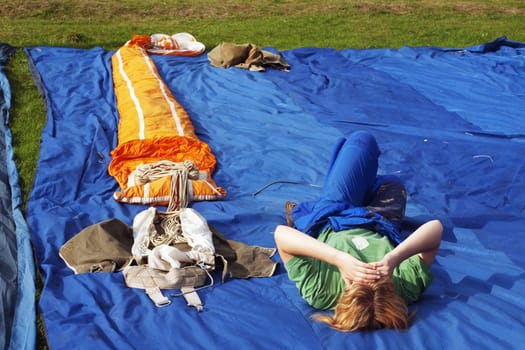 The girl lays near to the straightened parachute on the earth and looks in the sky at girlfriends