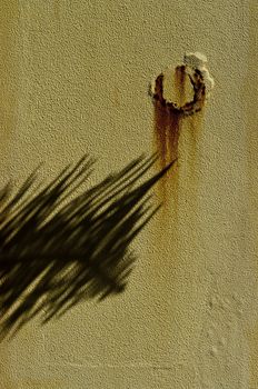 Abstract composition - yellow wall, shadow of a leaf, rust stains.