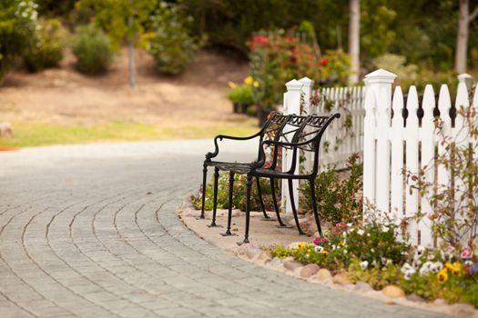 Iron Park Bench near a White Picket Fence in a Rural Setting.