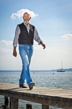 An old man with a grey beard is walking on a jetty