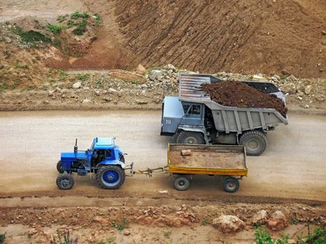 Tractor and heavy dumper on road in career.