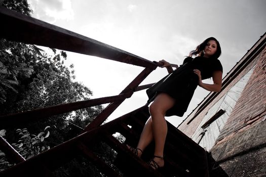 A young lady poses on a rusted old stairway in an urban setting.  Selective color.