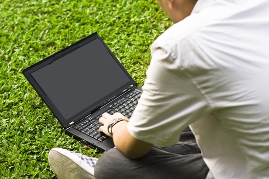 Man siting on the grass using laptop for texture