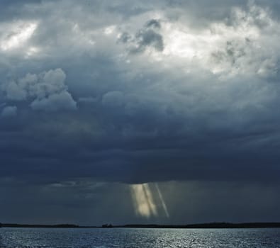 Thunderstorm over lake. Sun beams are visible through clouds