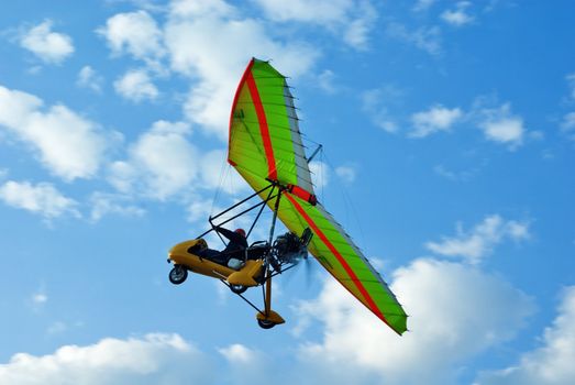 The motor hang-glider flies up in the blue sky