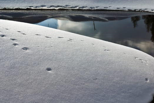Snowdrifts with traces and smooth water reflecting them