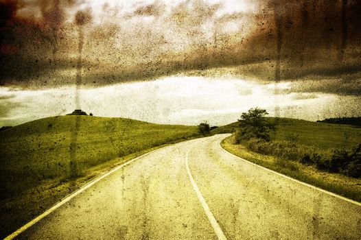 Road between fields under a cloudly sky