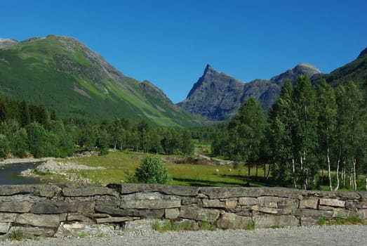 Beautiful Norway landscape with mountain peaks , river and old stone wall