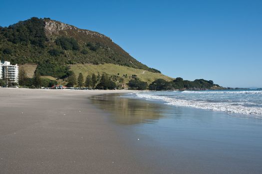 Mount Maunganui beach, with the Mount at end, under clear blue summer sky.