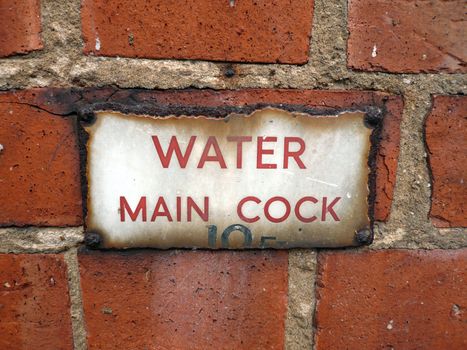 Red brick wall with aged water mains sign that has rusted
