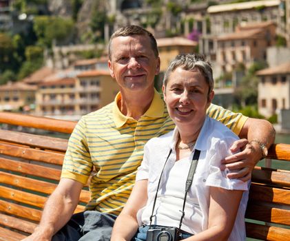Middle aged couple on a wooden seat on a boat on Italian lake with the ancient houses in the background. Smiling and facing the camera.