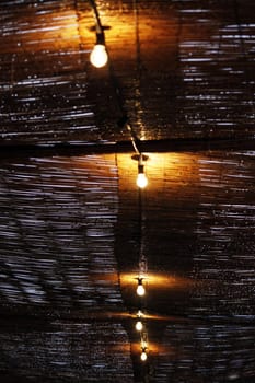 View of a wet bamboo ceiling with lightbulbs lit on the center.