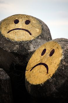 Close up detail of two painted smileys on a concrete rock.