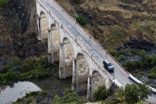 Top view of a arc stoned bridge over a river with a car passing by.