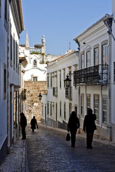 View of a historical street of the city of Faro in Portugal, with tourist silhouettes passing by.