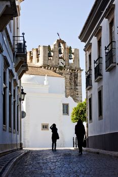 View of a historical street of the city of Faro in Portugal, with tourist silhouettes passing by.