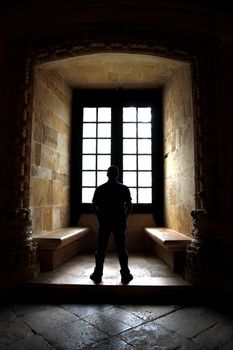 View of a lonely man facing a window inside a convent.