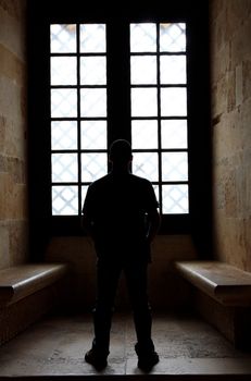 View of a lonely man facing a window inside a convent.