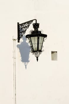 View of an old styled urban street light attached to a white wall.