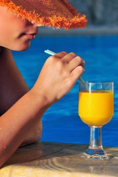 Beautiful woman by the pool, in straw hat, ready to enjoy a cool glass of orange juice