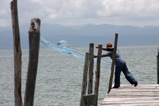 The fisherman he's fishing on the wooden bridge.