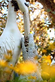 Crazy statue of a stork feeding a croc, on a autumn leaf surrounding setting, with snails on a garden of Faro, Portugal.