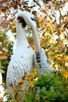 Crazy statue of a stork feeding a croc, on a autumn leaf surrounding setting, with snails on a garden of Faro, Portugal.
