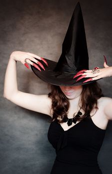 Pretty young witch with black hat and long nails
