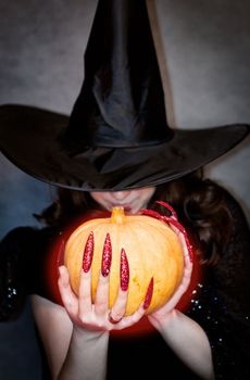 Pretty young witch with black hat, long nails and pumpkin