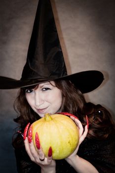 Pretty young witch with black hat, long nails and pumpkin