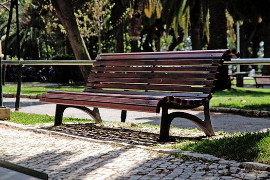 View of an empty wooden park bench in the city of Faro, Portugal.