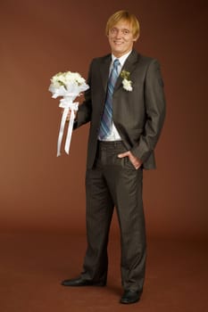 Happy groom with a bouquet on brown background